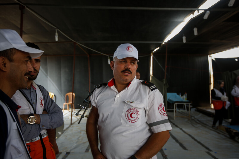 Man in paramedic uniform with a metal splint on his arm is seen from waist up while standing in field medical tent