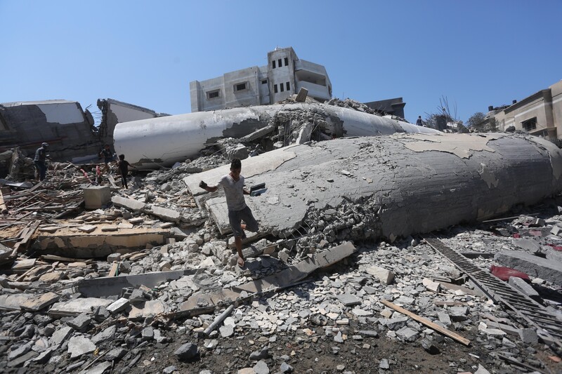 Boy carrying books walks along rubble of destroyed building