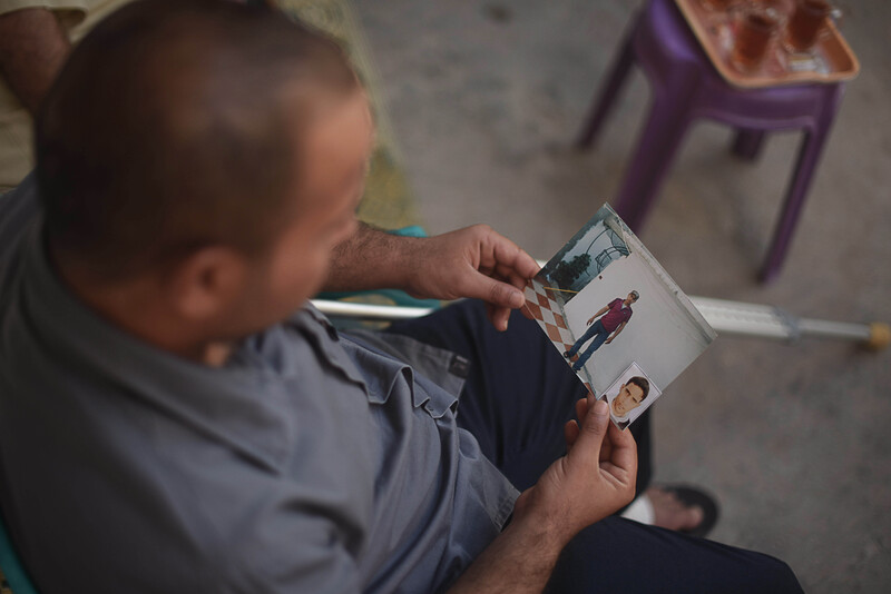 Photo taken from above shows sitting man looking at two photographs he is holding