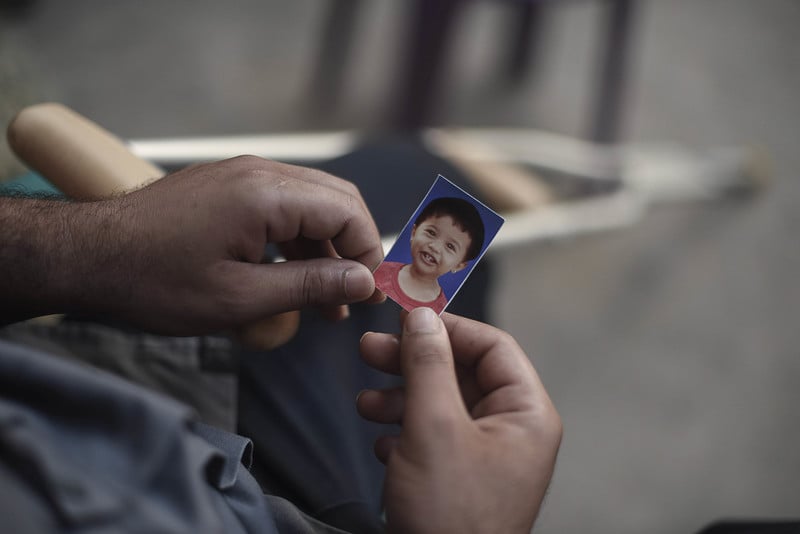 Close-up photo of two hands holding a passport-size image of a smiling baby