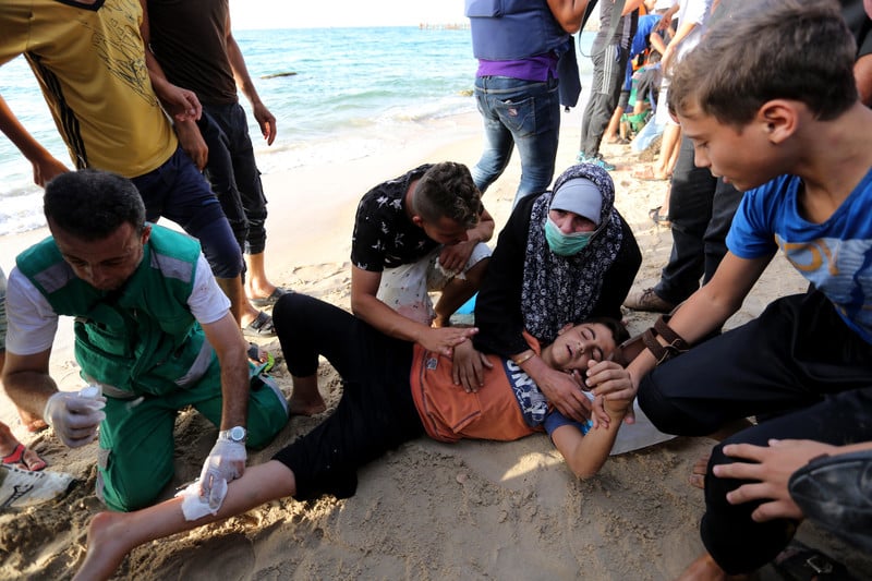 Men and women provide first-aid to a child lying on the beach with a bandage on his leg 