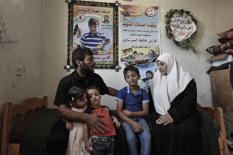 A woman and man sit on a twin-sized bed with three children and posters honoring their slain son on the wall behind them