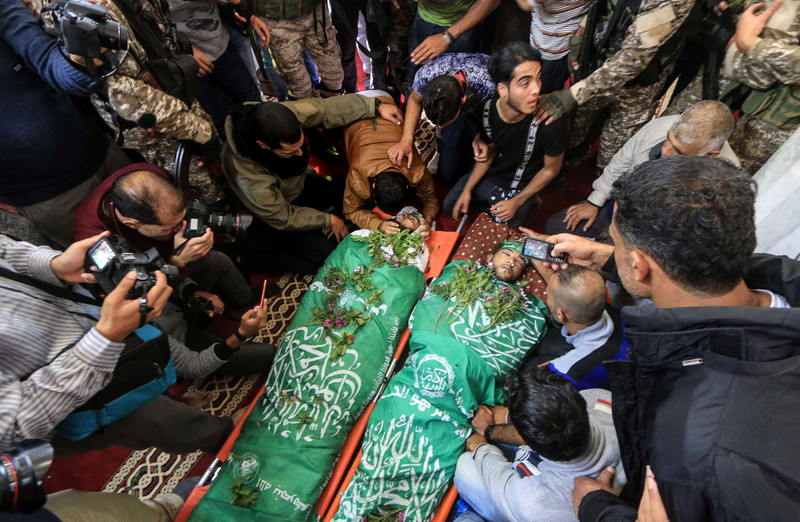 A crowd surrounds the bodies of two young men wrapped in Hamas flags and covered with flowers