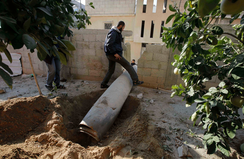 A Palestinian man steps over an unexploded missile around two meters long 