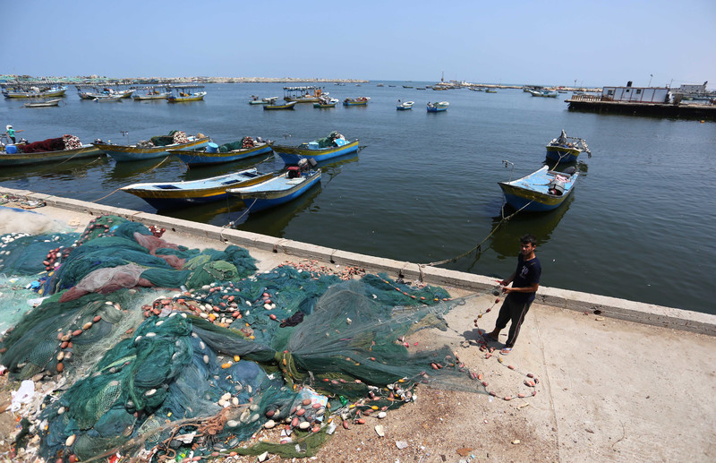 A young man pulls on a pile of fishing nets while standing next to docked boats