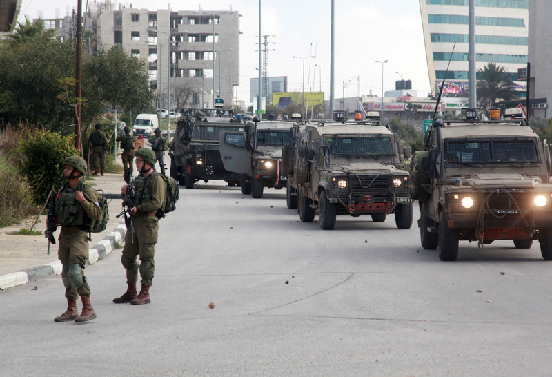 Israeli soldiers stand near four jeeps on road littered with stones