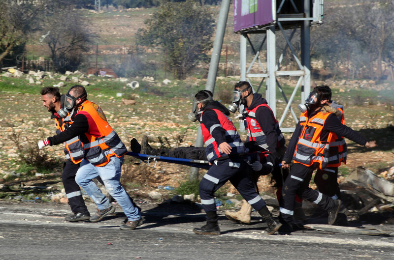 Six paramedics, some wearing gas masks, carry a person on a stretcher