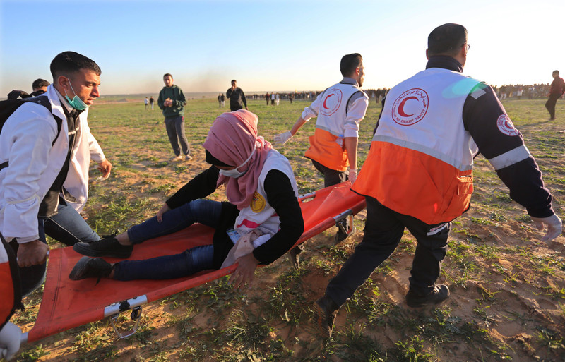 A woman grips her leg while being carried on a stretcher by three paramedics