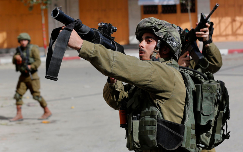 Two Israeli soldiers point their weapons at Palestinian demonstrators.