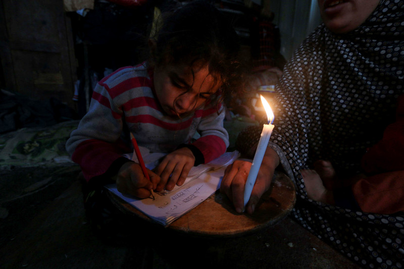 A Palestinian boy poses behind candles during a power outage