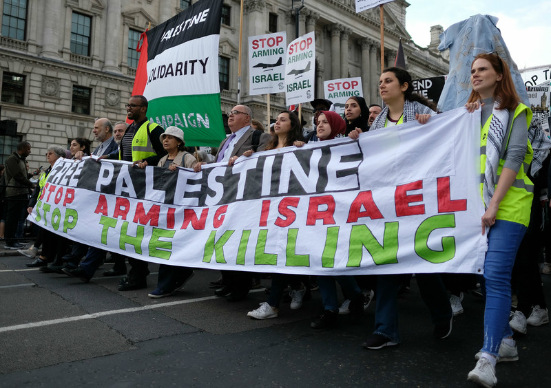 Marching near the British Parliament, protesters hold a large banner that says "Free Palestine, Stop Arming Israel, Stop the Killing"
