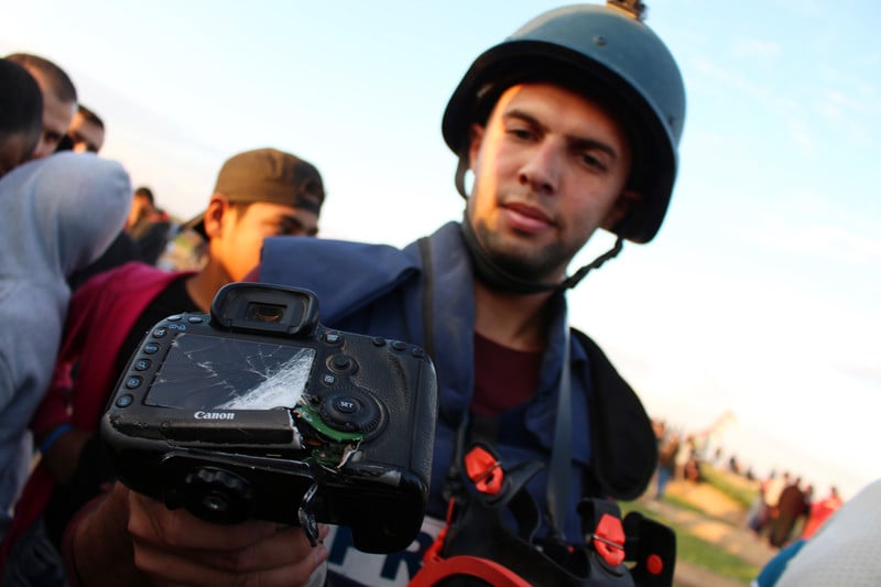 Journalist wearing helmet and flak jacket displays a badly damaged camera 