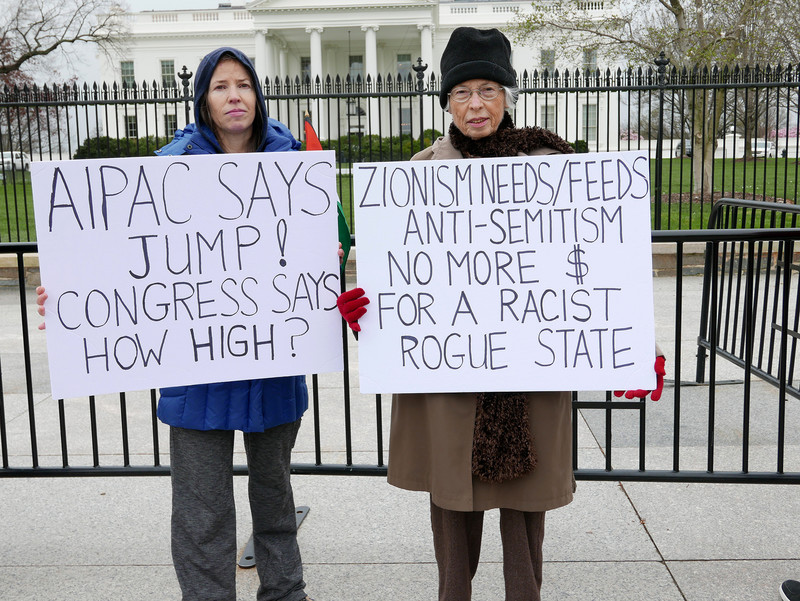 Protesters stand in front of the White House with signs reading "AIPAC says jump! Congress says how high?" and "Zionism needs/feeds anti-Semitism, no more $ for a rogue racist state"