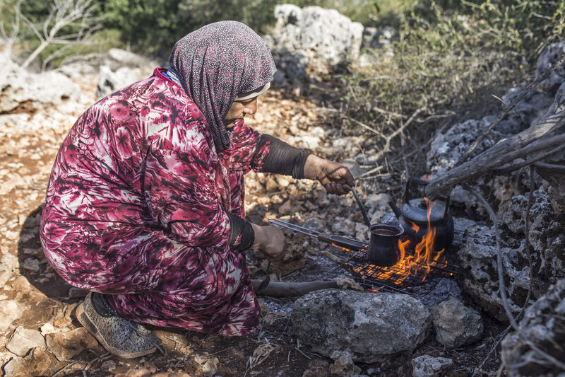 A woman prepares coffee over an open fire. 