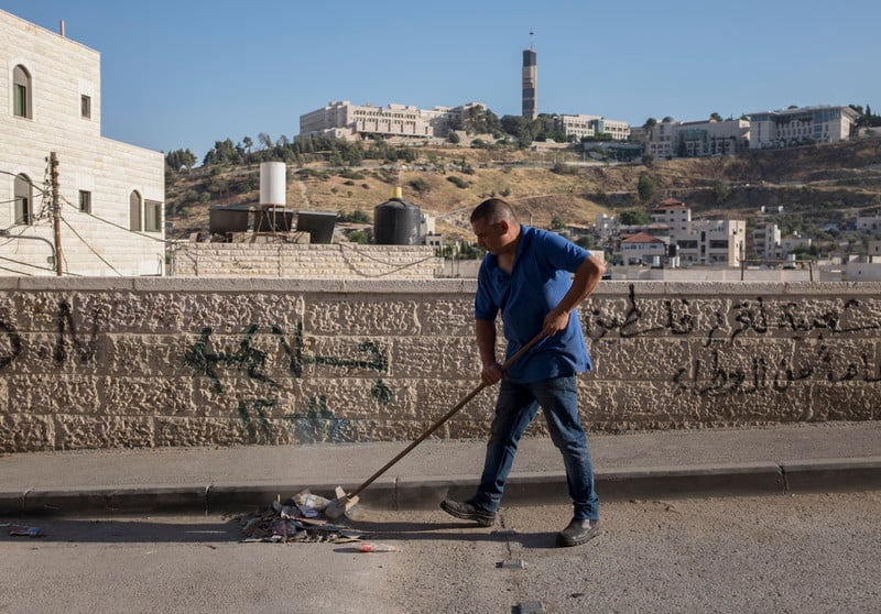 A shopkeeper sweeps the street in Izzawiyeh. 