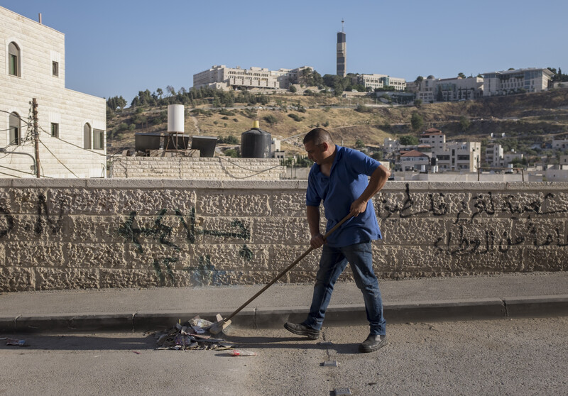 A shopkeeper sweeps the street in Izzawiyeh.