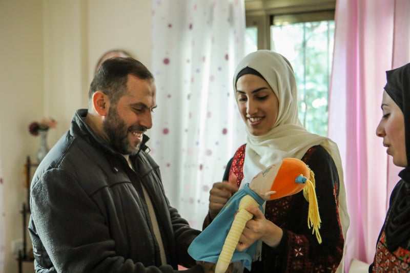 A smiling Imad al-Din al-Saftawi looks at a plush doll held by a smiling young woman