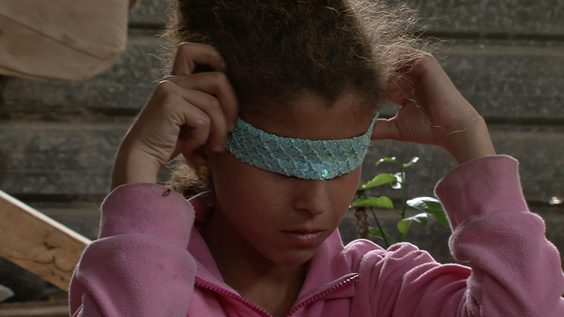 A young girl wraps a sequinned headband over her eyes