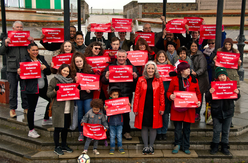 A group of Labour activists hold red signs in support of their prospective candidate for Member of Parliament.