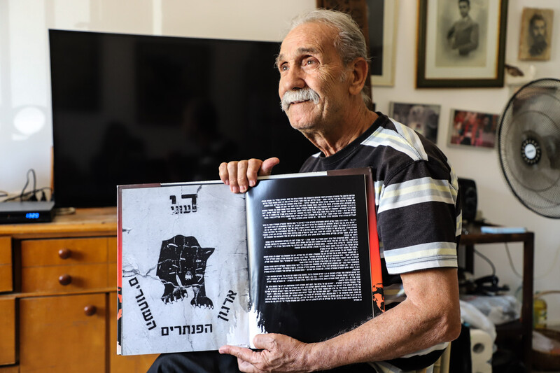 Black Panther founder Reuven Abergel sits with a book open on a page displaying the logo: "Enough with poverty!"