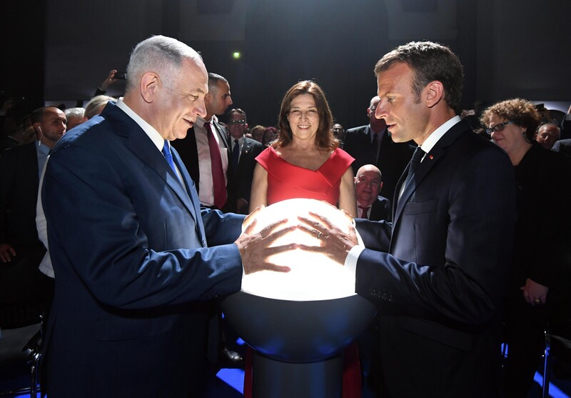 Two men face each other with their hands on a glowing orb, as a woman looks on