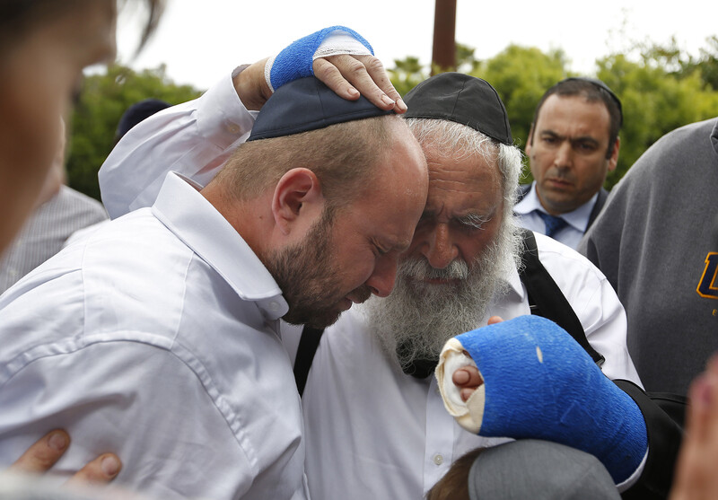 Two men, one with bandaged hands, embrace, as others look on.