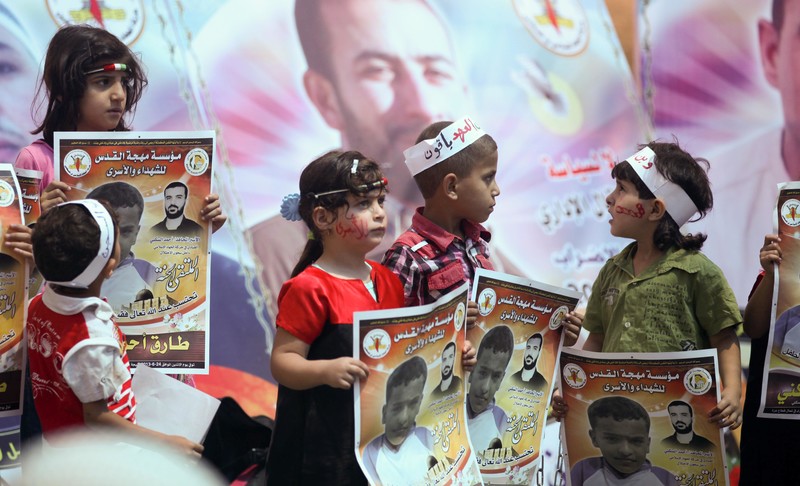 Four children wearing headbands hold up posters depicting a child and bearing text calling for the release of prisoners