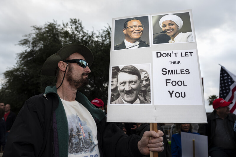 A man holds sign with pictures of Ilhan Omar and Hitler