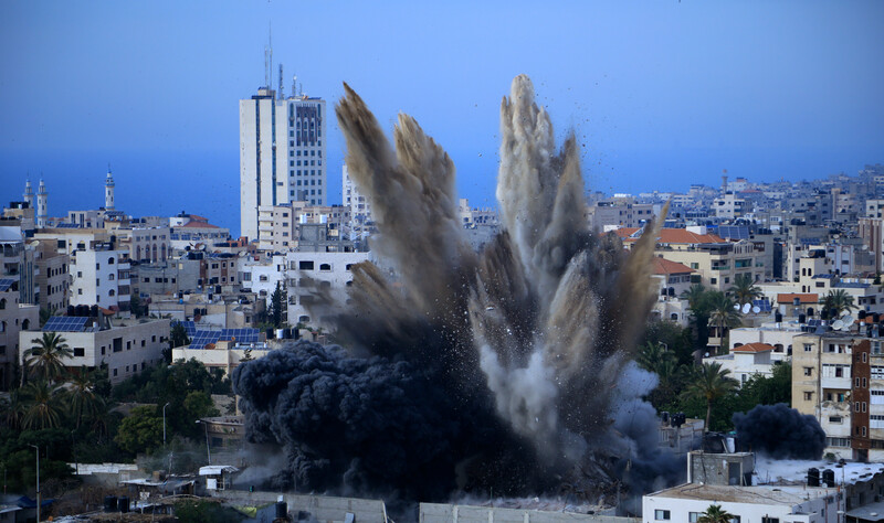 Smoke rises over buildings against Gaza skyline. 