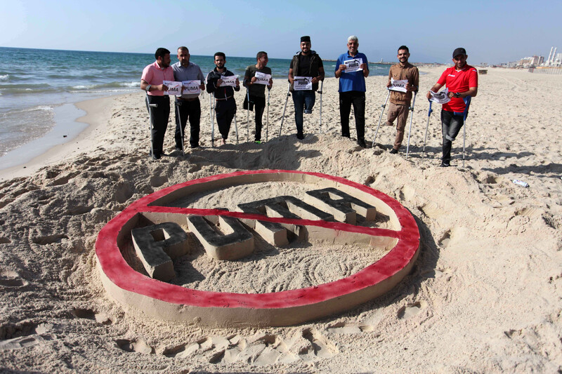 Men who lost their legs holding signs near a sand structure on the beach. 