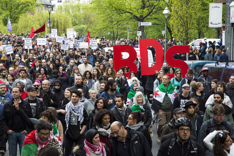 Hundreds of people march, some with signs that say "BDS"