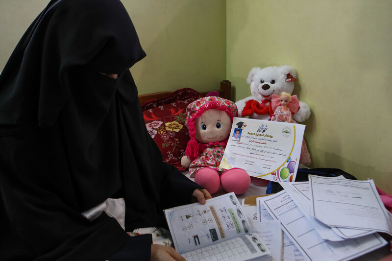 A veiled woman sits on a bed with children's books and toys