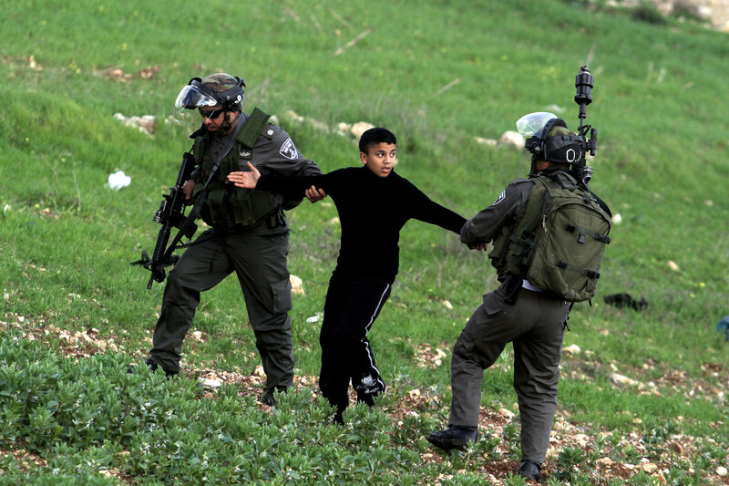 Two Israeli soldiers pull on the arms of a Palestinian youth.