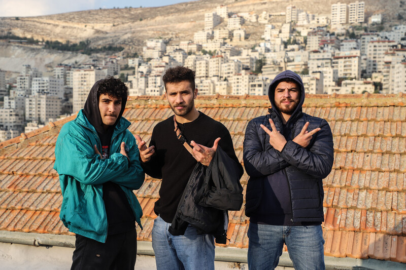 Three men look at camera making signs with their hands. 