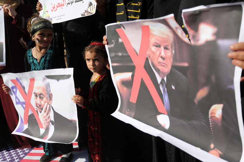 Girls hold signs with faces of Donald Trump and Benjamin Netanyahu crossed out.