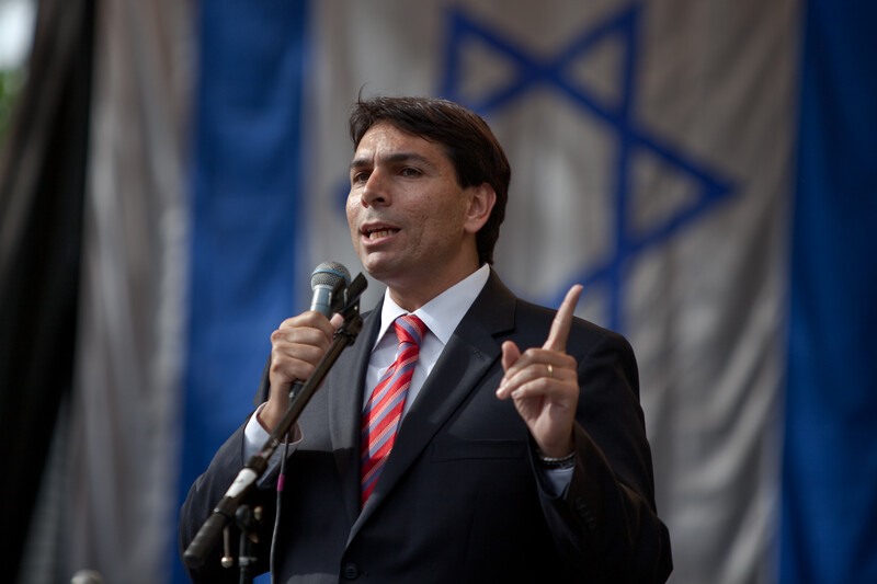 Man holds microphone in front of Israeli flag