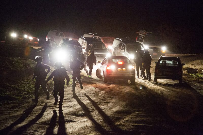 Armed police run in front of cars with the headlights on at night