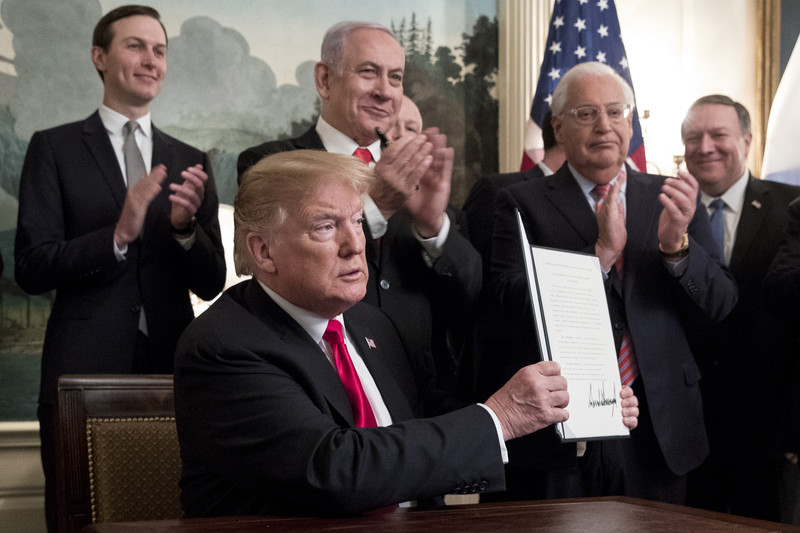 Four standing men applaud another man sat at a desk holding up a piece of paper.
