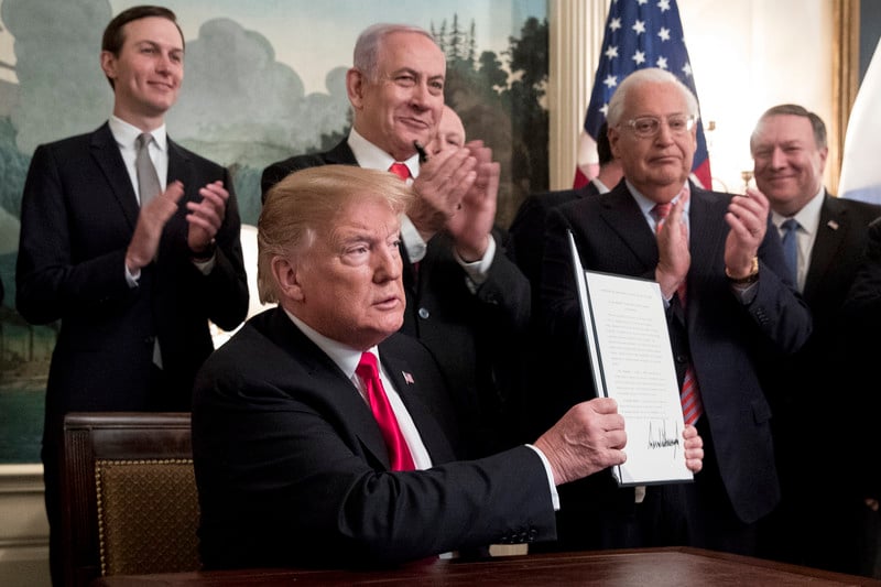 Four standing men applaud another man sat at a desk holding up a piece of paper.