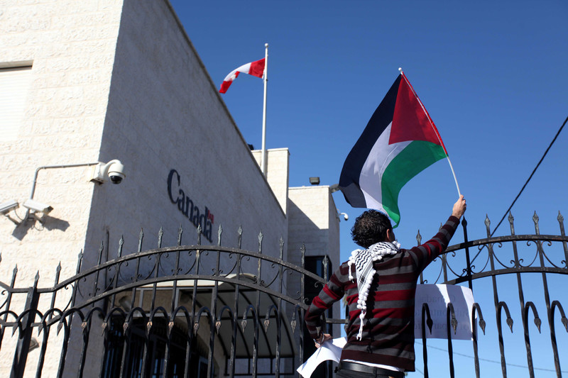 A protester waves a Palestinian flag over the gate of the Canadian embassy in Ramallah.