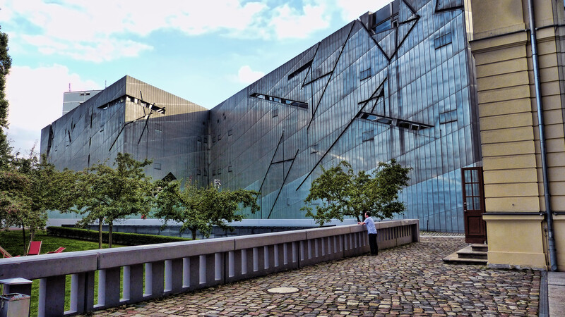 A man is dwarfed by a building that has many angles in its glass facade.