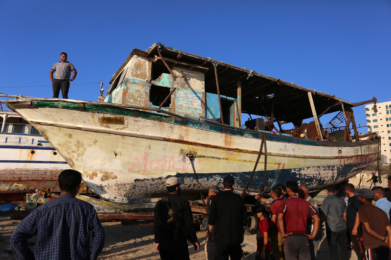 Crowd stands around dilapidated boat