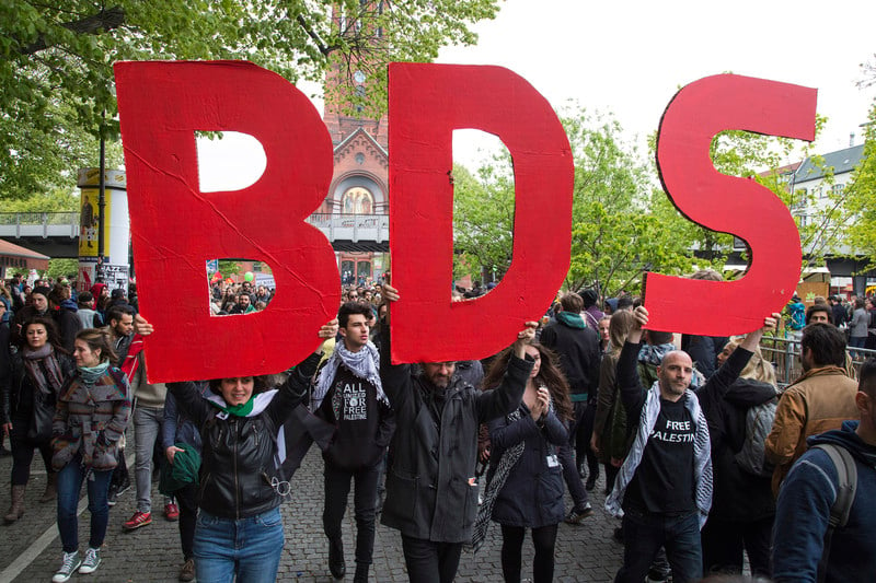 Protesters hold up big letters that spell BDS 