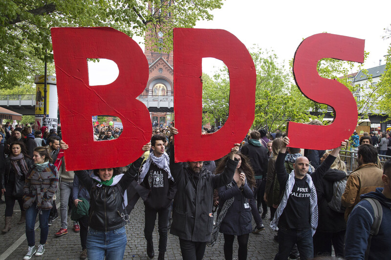 Protesters hold up big letters that spell BDS 