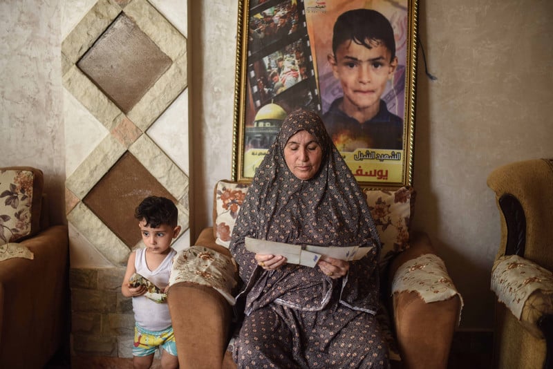 Woman sits in front of poster commemorating killed boy