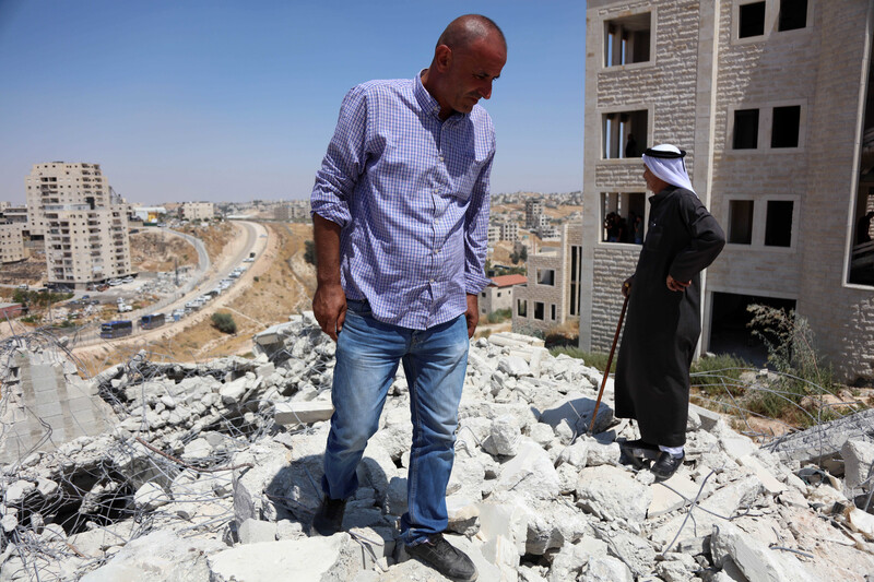 Two men looking in different directions stand atop rubble