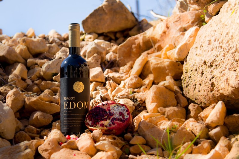 A wine bottle and a pomegranate are perched on some rocks.