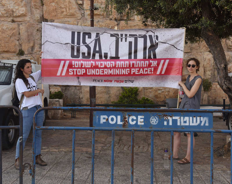 Two women hold up a sign reading "USA stop undermining peace" in English and Hebrew