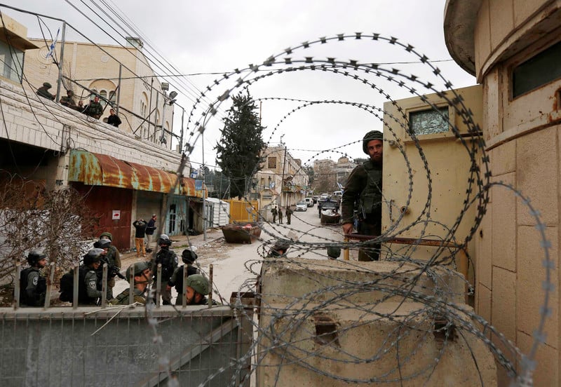 Soldiers seen behind barbed wire and walls with closed shops behind