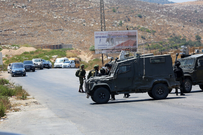 Parked jeep and soldiers stand in the middle of the road